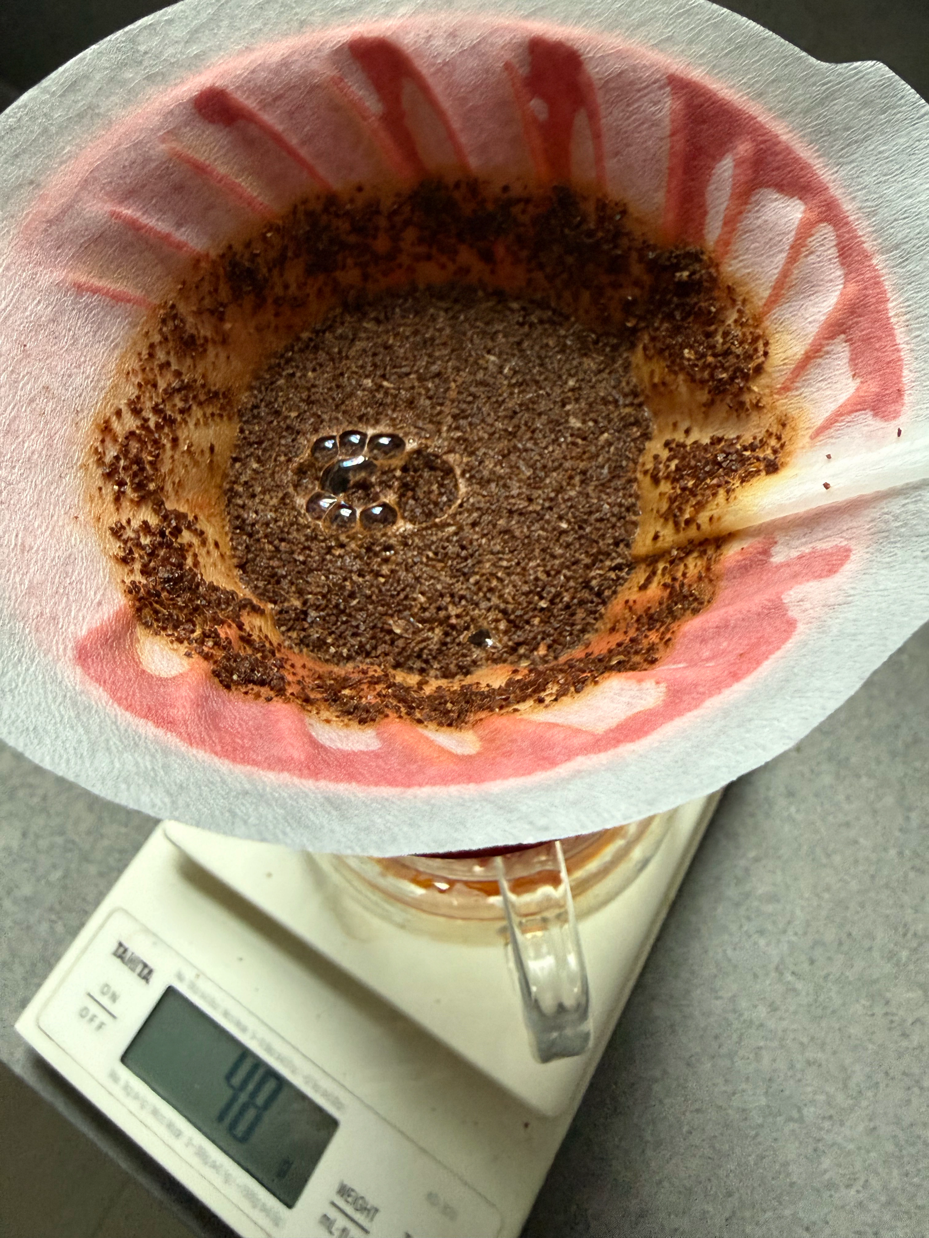 Coffee brewing in a paper filter in a red V60, above a glass server and digital scale.